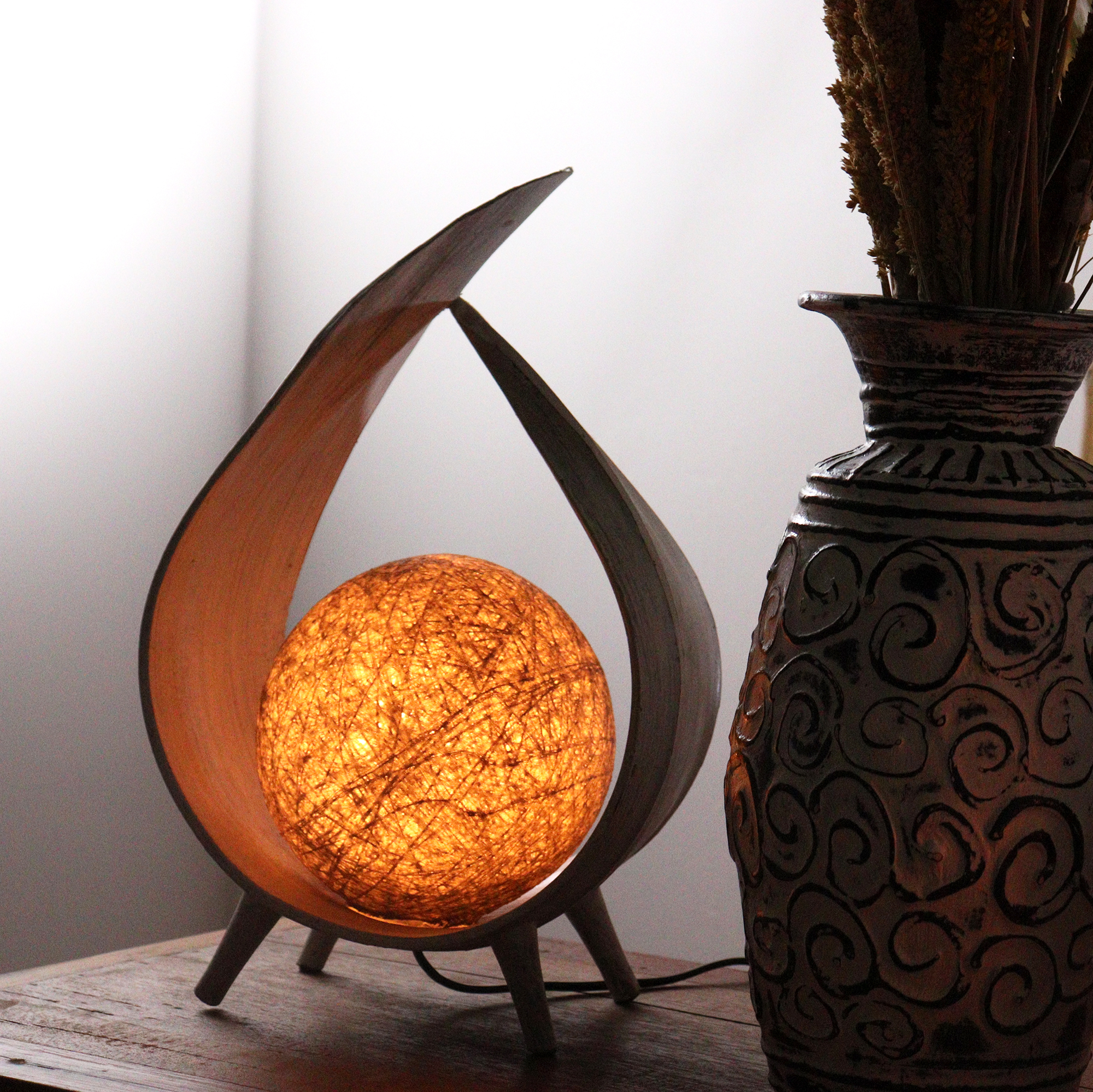 Artisan-crafted coconut glow lamp with curved wooden stand and glowing spherical coconut leaf shade